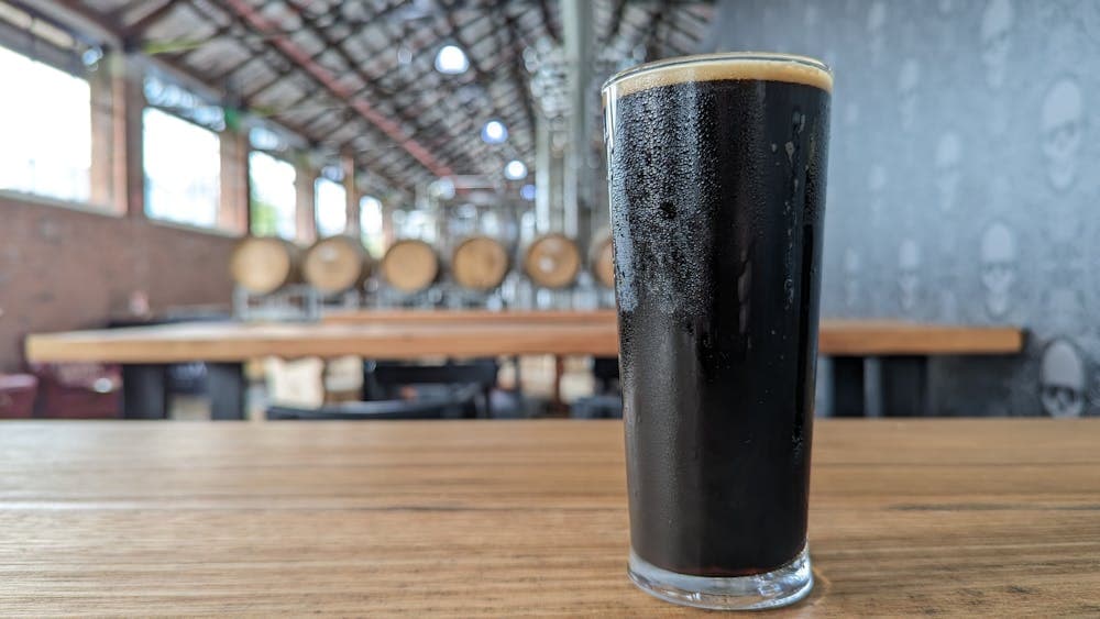 Glass of dark beer in focus with brewery and barrels blurred I'm the background
