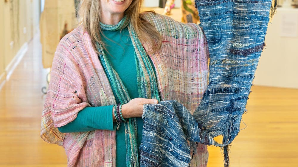 Prue Simmons holds a blue SAORI woven wall hanging in an exhibition gallery