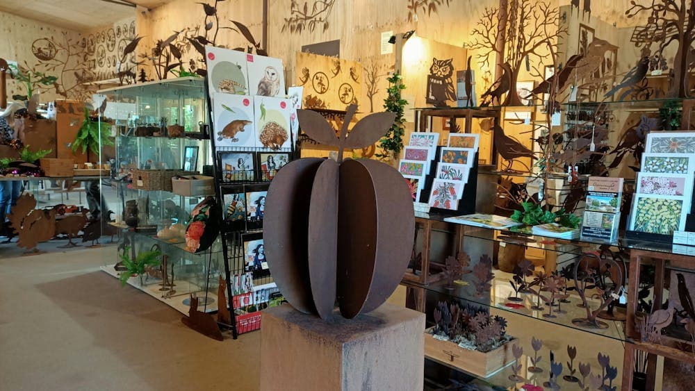 A large metal apple sites on a plinth, surrounded by other metal art and some floral prints & cards.