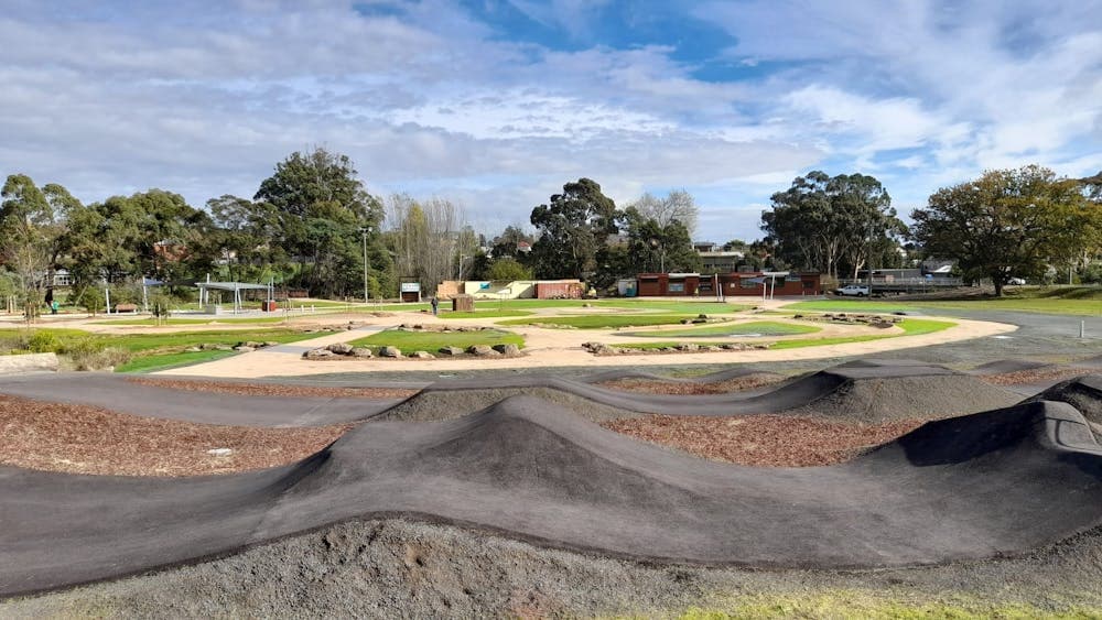 A view across a bitumen pump track, dirt learn to ride track and playground equipment