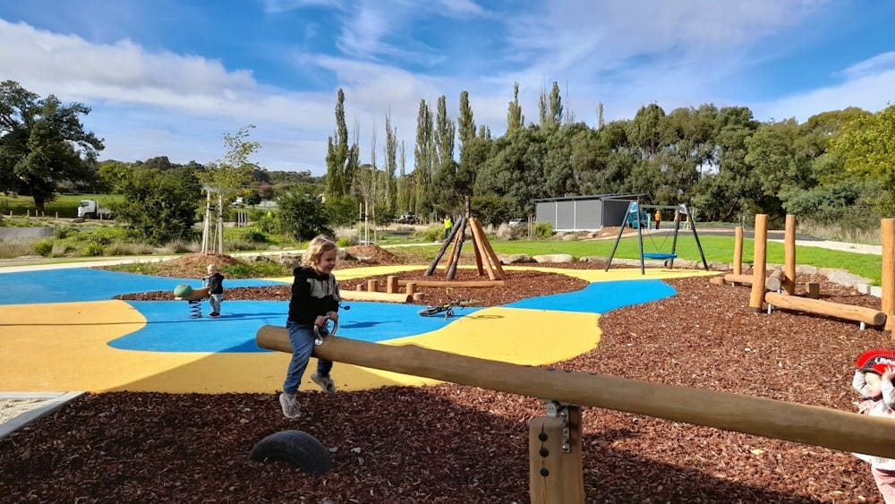 A sunny day looking across a playground with a small child on a wooden seasaw