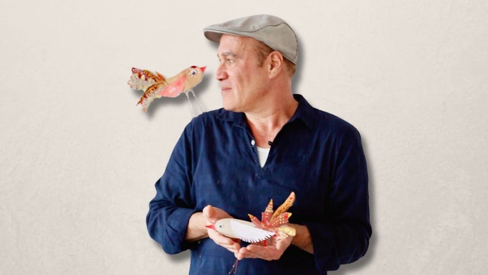 An image of Yuval Zommer holding a paper bird, and looking over his shoulder at another paper bird
