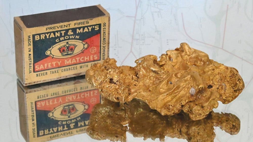 A photograph of a gold nugget with an old matchbox next to it for scale