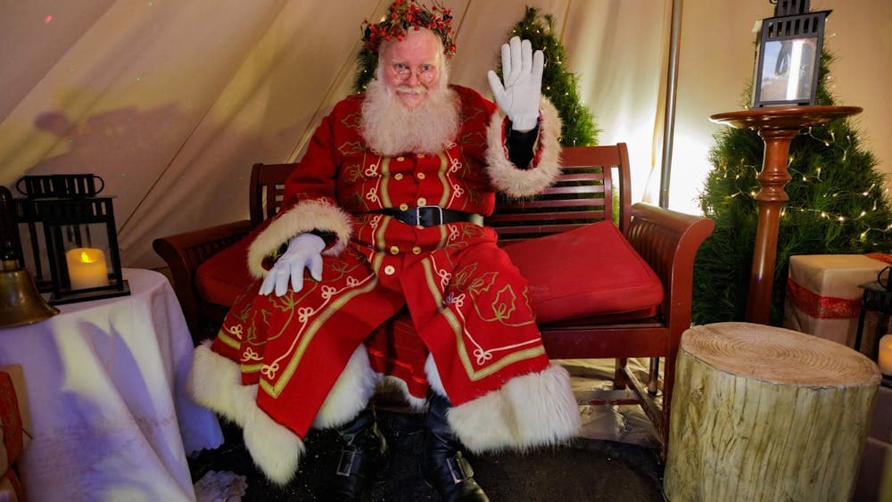 St Nicholas wearing red and white outfit seated and waving inside hut
