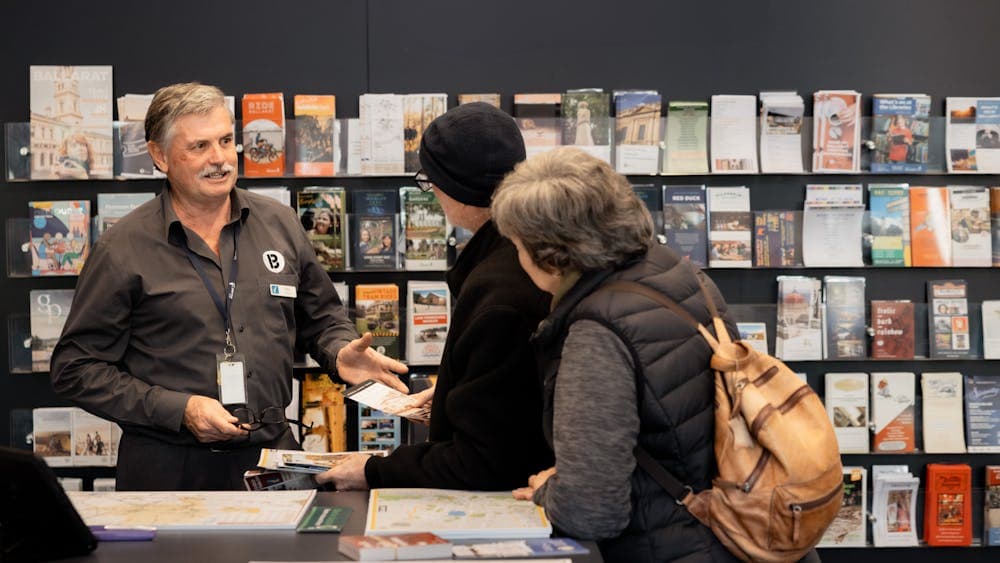 Rick standing in front of a brochure wall, helping two visitors