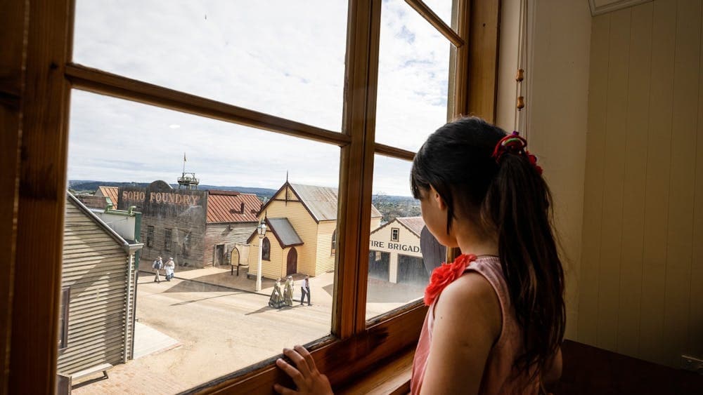 Girl looking outside window with view over Sovereign Hill Main Street