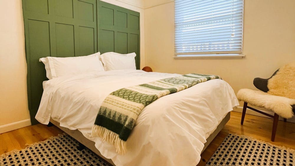 Queen bed, blanket, green headboard, window.