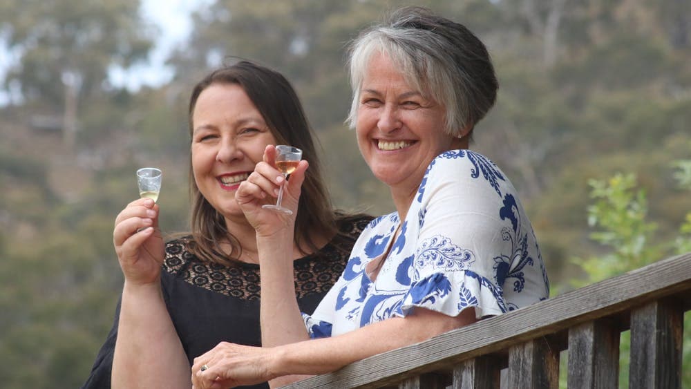 Two women smiling, raising gin liqueur glasses