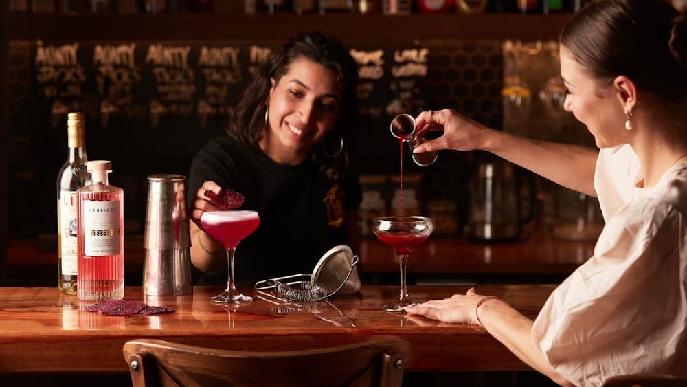 lady pouring a cocktail in the glass while another lady garnishes a drink at the bar table