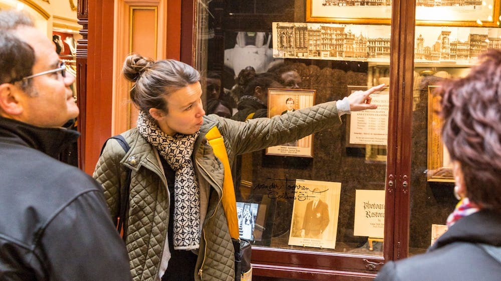 Woman stands pointing to historical photos, as she shares with another person, They are in an arcade