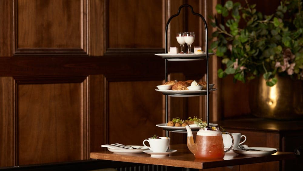 high tea set up on a table with food on high tea trays and cups of tea around it