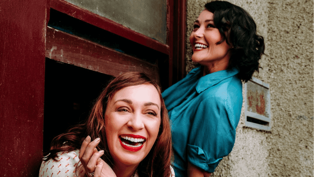 Two young women from 1937 leaning out a window laughing