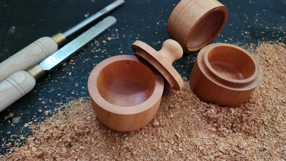Two small wooden round boxes surrounded by wood shavings and tools