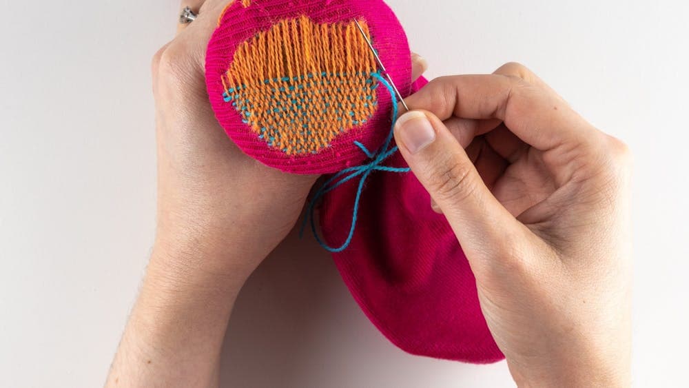 Close up of a pair of hands repairing pink and orange knitwear
