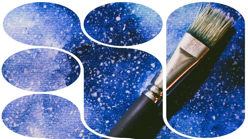 An image of an artists paintbrush resting on a dark blue picture with white splatter stars