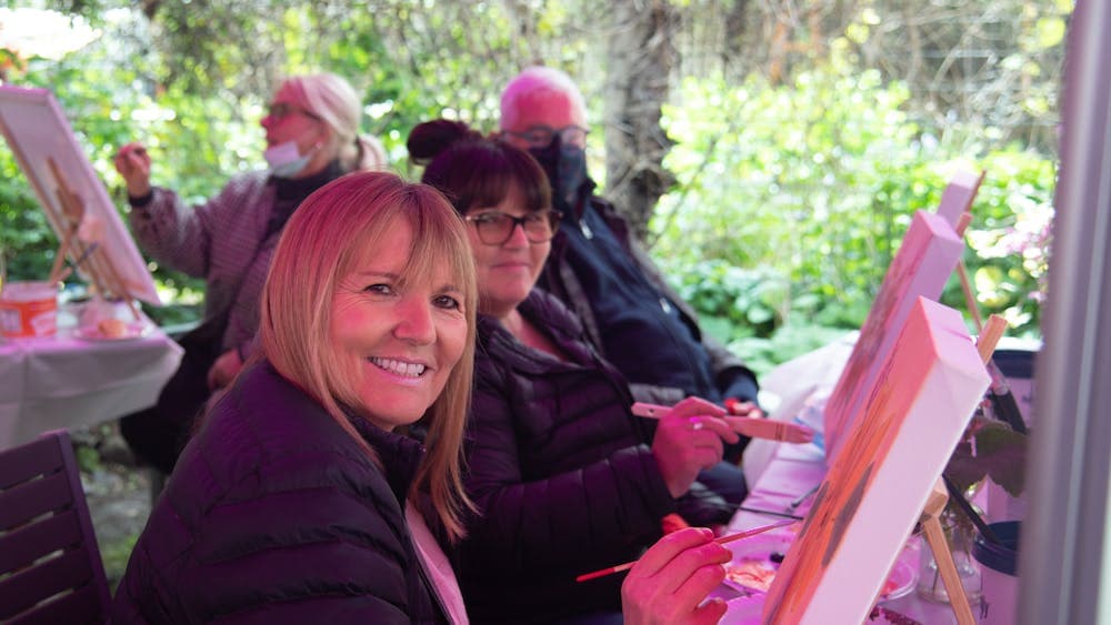 Two smiling women in a garden setting painting on small easels.