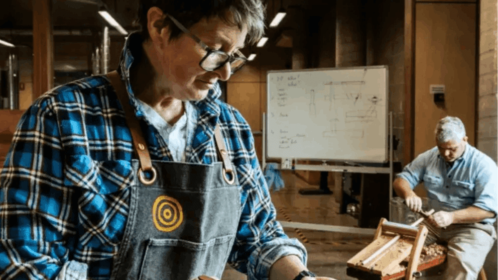 Two men carving wood for chairs in a workshop