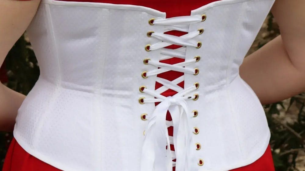 Backshot of a woman wearing a white underbust corset from behind with red top underneath