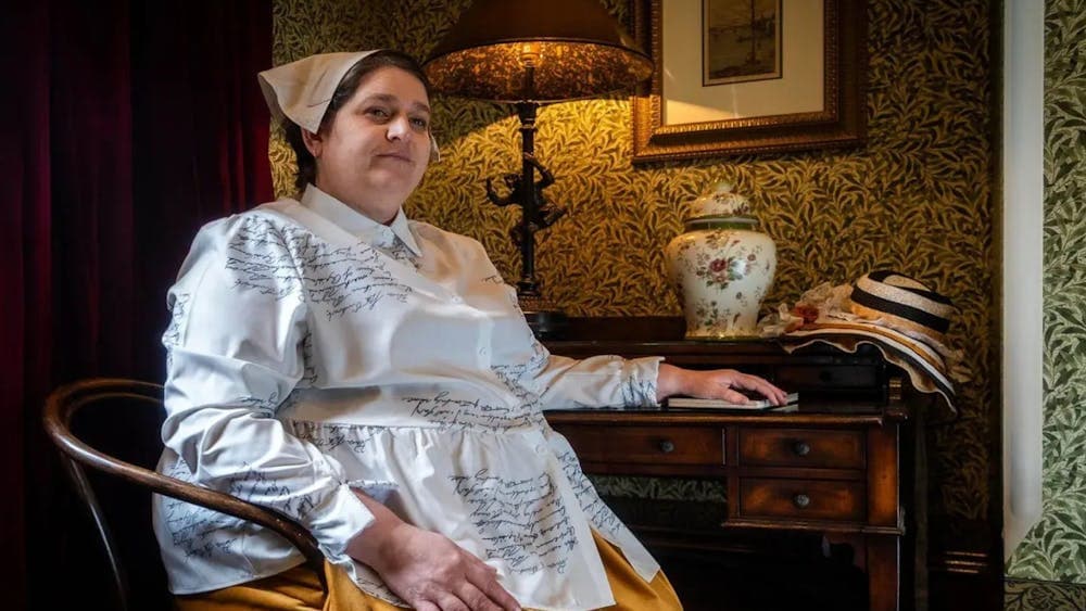 Performer Megan J Riedl  dressed in 19th century costume seated at table