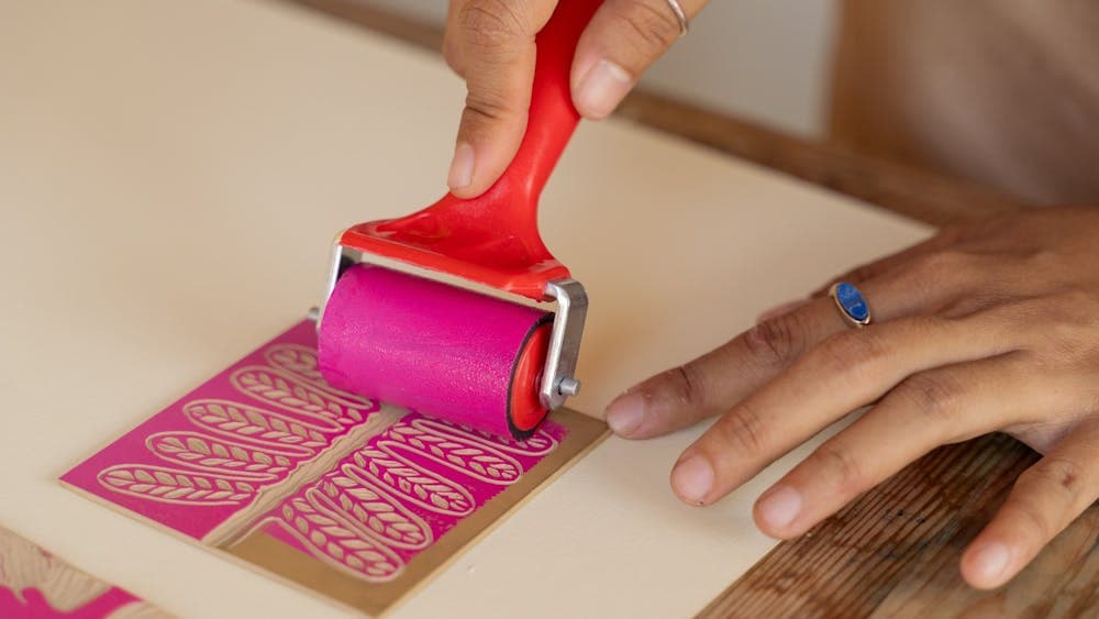 Hands rolling pink paint on floral pattern on paper