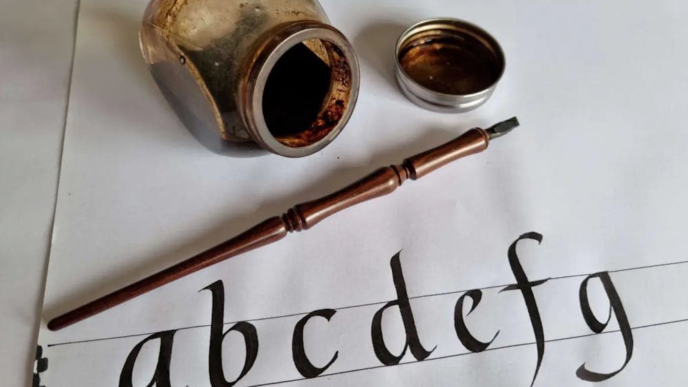 Letters of alphabet in calligraphy on paper with ink well and pen