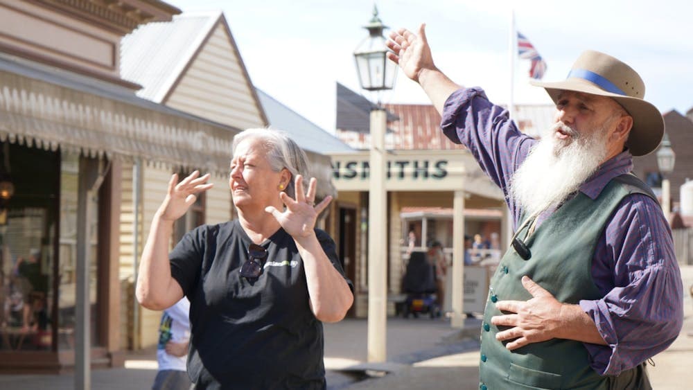 Man in historical costume pointing to a Sovereign Hill building with a woman interpreting in Auslan