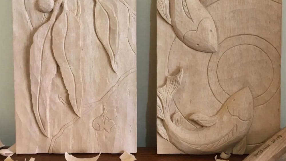 Two wooden relief carvings of gum leaves and koi fish