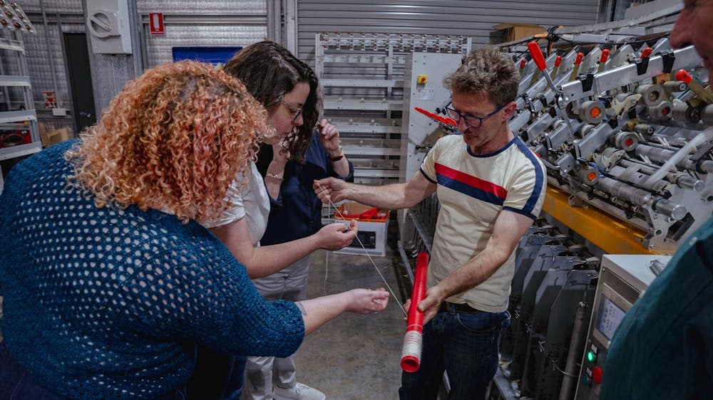 4 people looking at a single strand of yarn which has just been spun