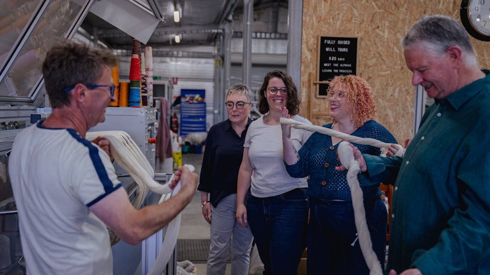 a group of people are standing together with 1 person twisting a yarn into a skein