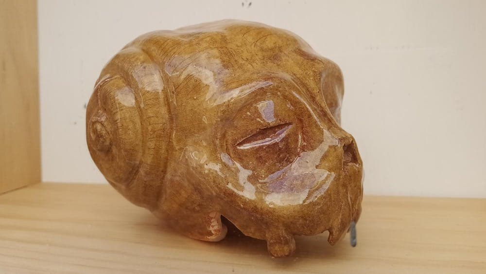Ceramic sculpture of a morphing skull with a golden brown colour placed on a shelf.