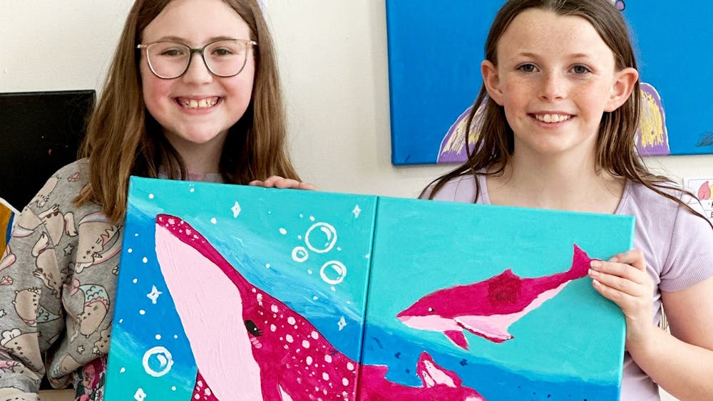Friends showing a canvas painting of whales that they have painted together