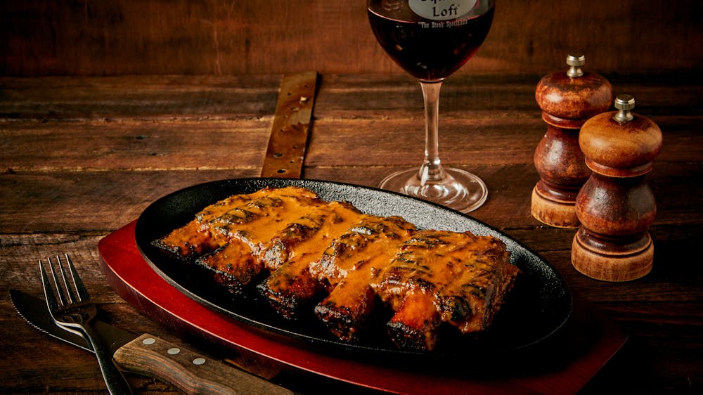 Beef Ribs on a plate with salt and pepper shakes and a glass of wine in the background