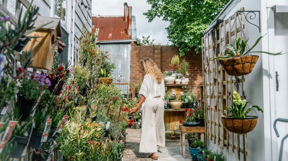 A woman wearing natural linen top and pants, looking at plants in a nursery.