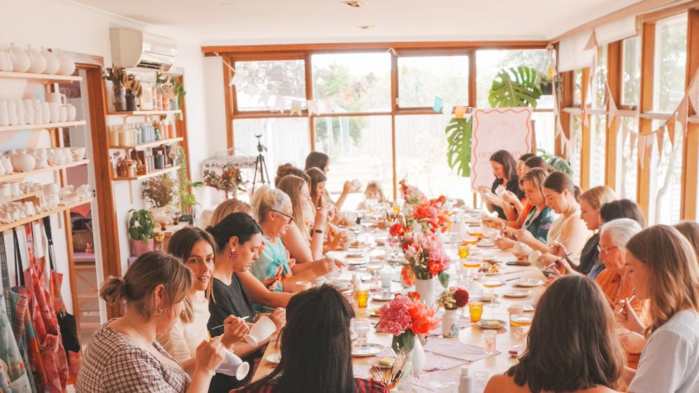 A group of artists painting pottery at a large table
