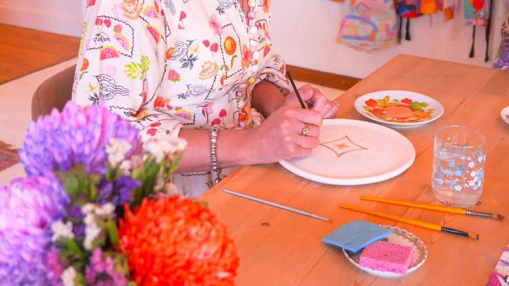 An image of a woman in a floral dress painting a plate