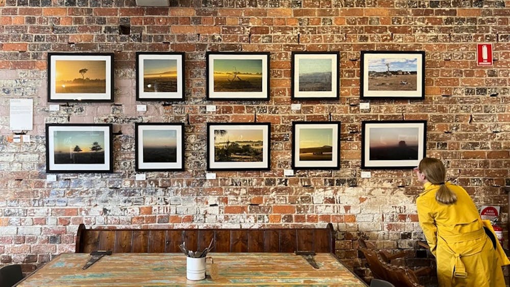 Woman in a yellow coat looking at an exhibition of 10 photographs hanging in a cafe venue.