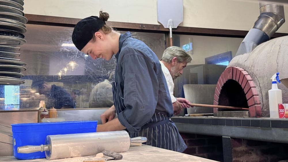A chef preparing pizza dough on a bench in the Courthouse Hotel kitchen with a pizza oven in the bac