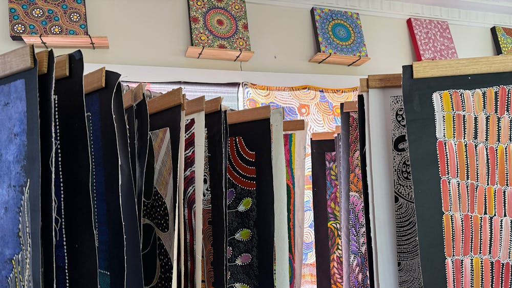 a large number of unstretched canvas painting hanging in front of small square paintings on the wall