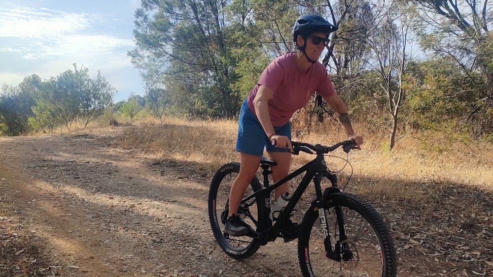 A women is standing on her pedals riding a mountain bike down a hill on a gravel track