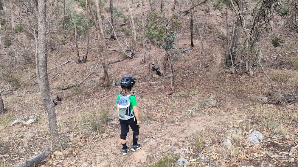 A young girl is walking down a singletrack dressed in mountain biking clothing