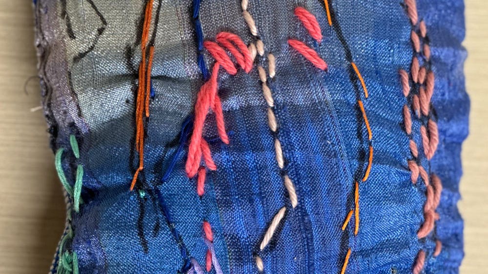 A blue fabric cushion with coloured stitching on the cover.