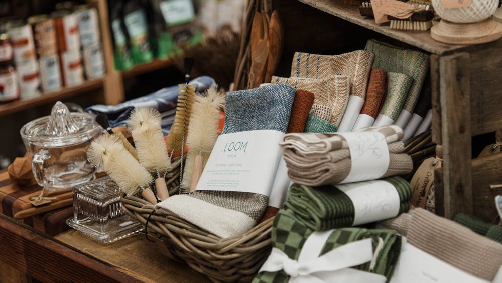 A basket full of hand woven cloths and cleaning bottle brushes on a shelf with glass butter dish