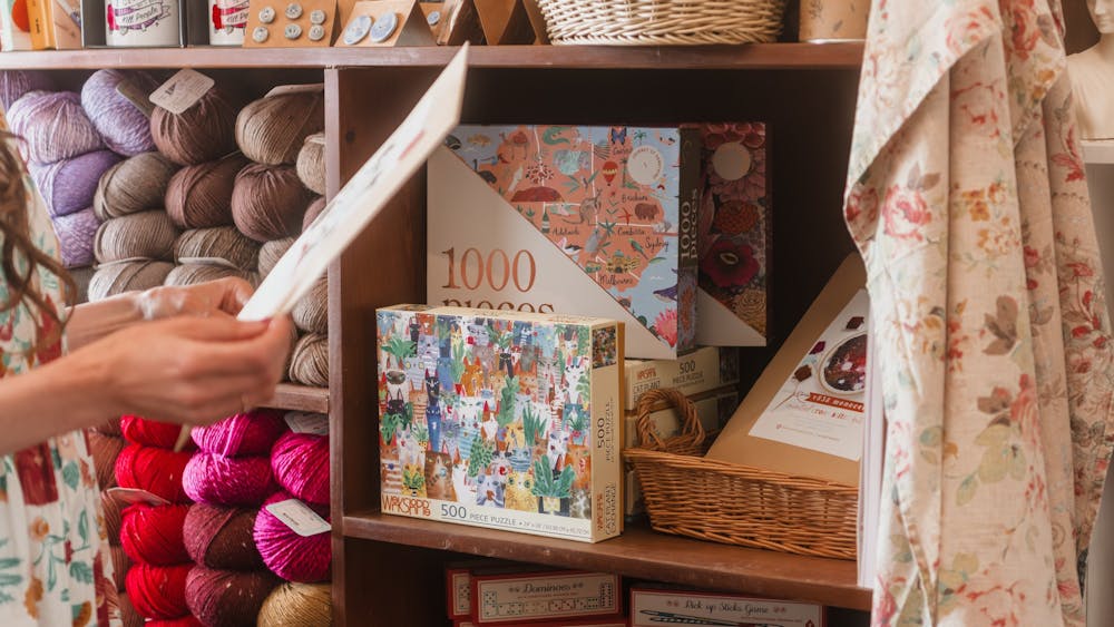 person holding a book near a shelf full of wool yarn and puzzles