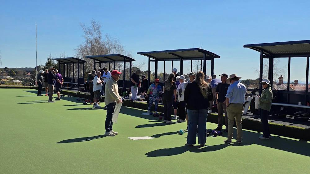People gathered on a new synthetic bowling green on a sunny day.