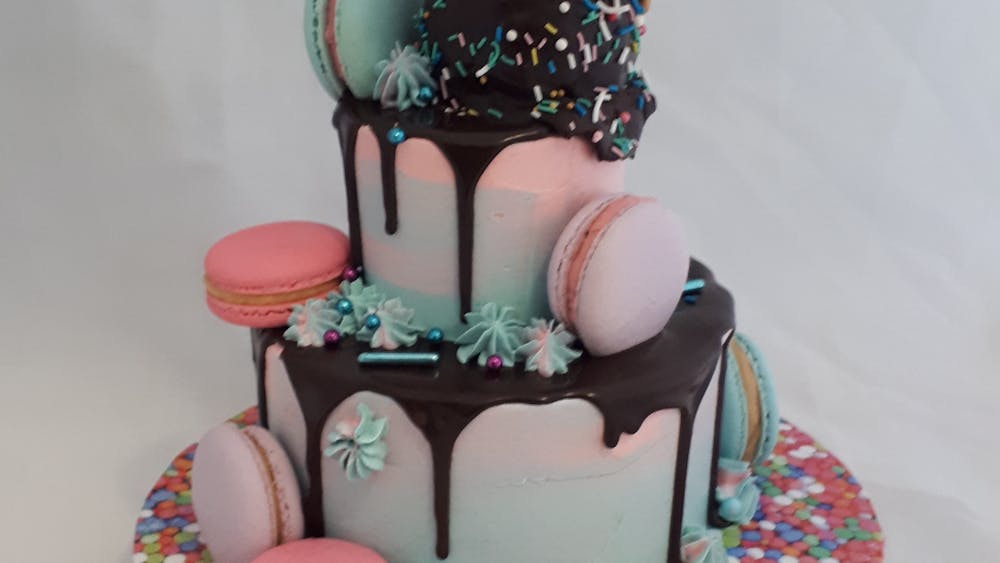 In tones of pink, blue and purple a two tier cake with macarons and an ice cream cone on top