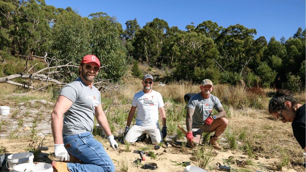 Three people pose planting trees.