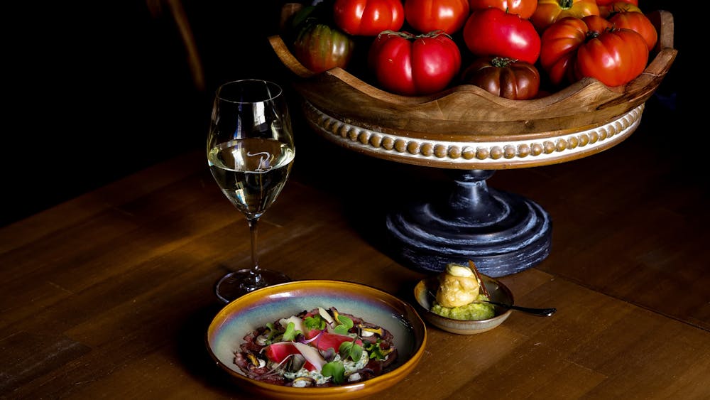 Plated dish and glass of wine placed next to a bowl of tomatoes